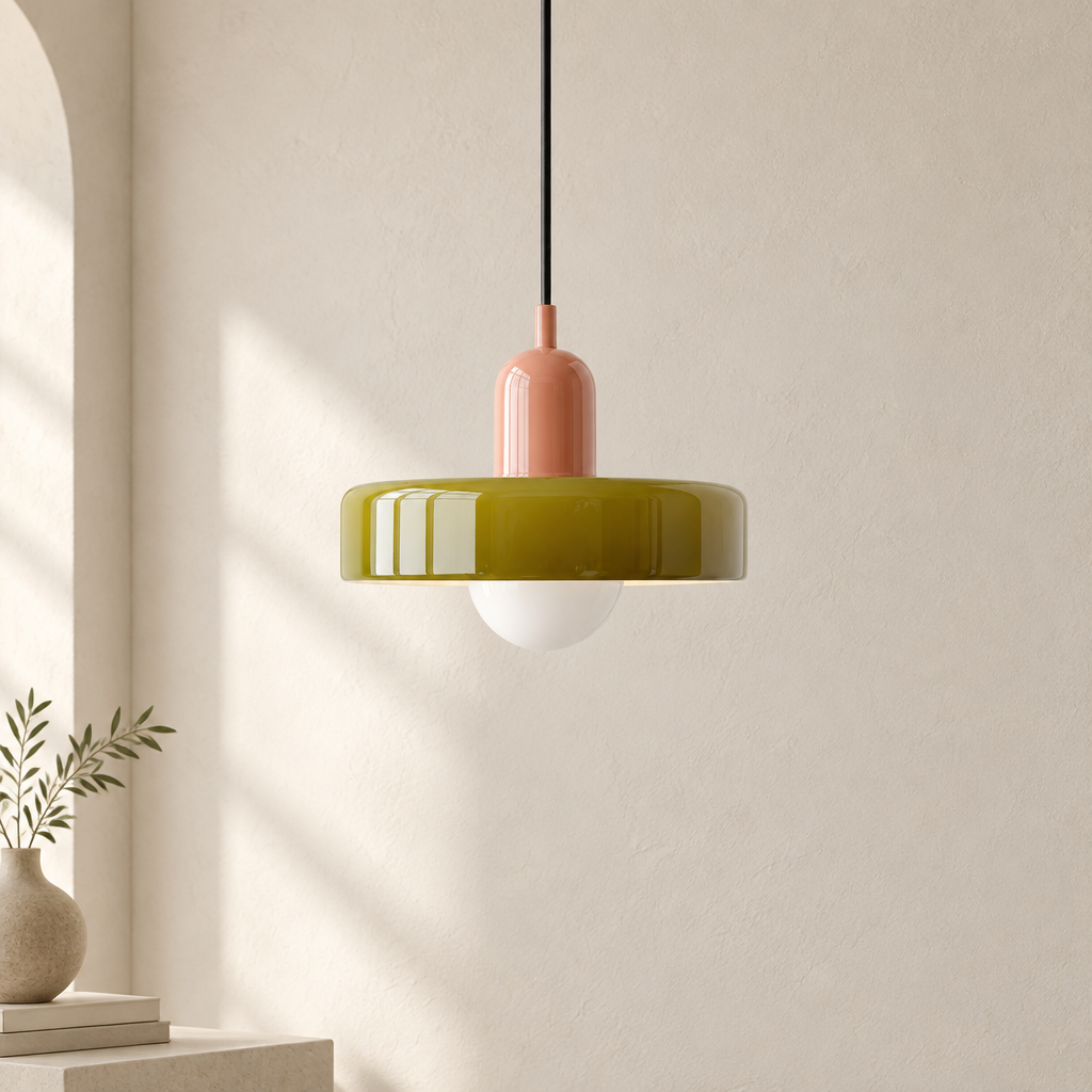 A modern pendant light with a glossy olive green top band, a matte dusty pink central neck, a black hanging cord, and a white frosted globe shade, shown in a minimalist room setting.