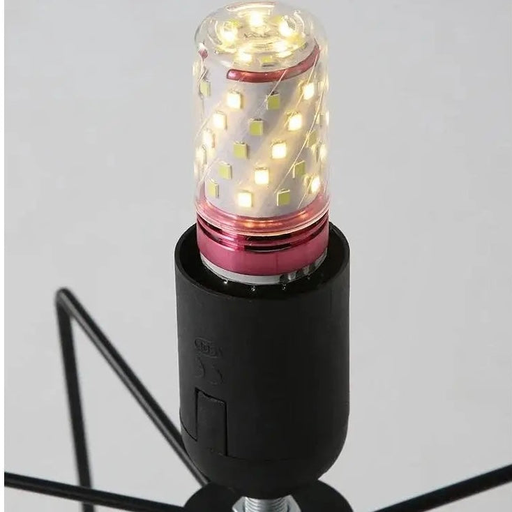 A close-up of a black lamp base with a spiral LED light bulb illuminated, showing warm white light points and a metallic pink accent ring, on a light gray background.