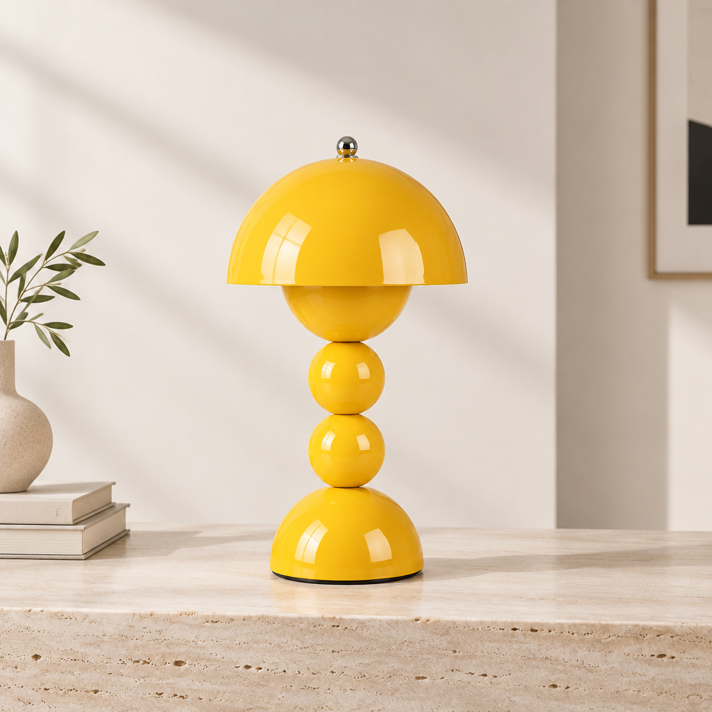 A glossy yellow table lamp with a dome-shaped shade and stacked spherical base, displayed on a light stone surface against a warm off-white wall.