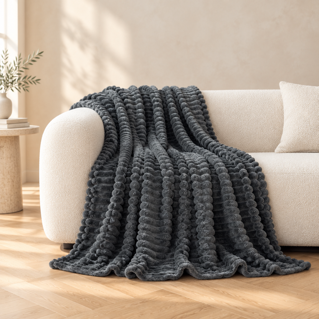 A dark charcoal-grey textured throw blanket draped over a cream-coloured sofa in a bright, modern living room with light wood floors.
