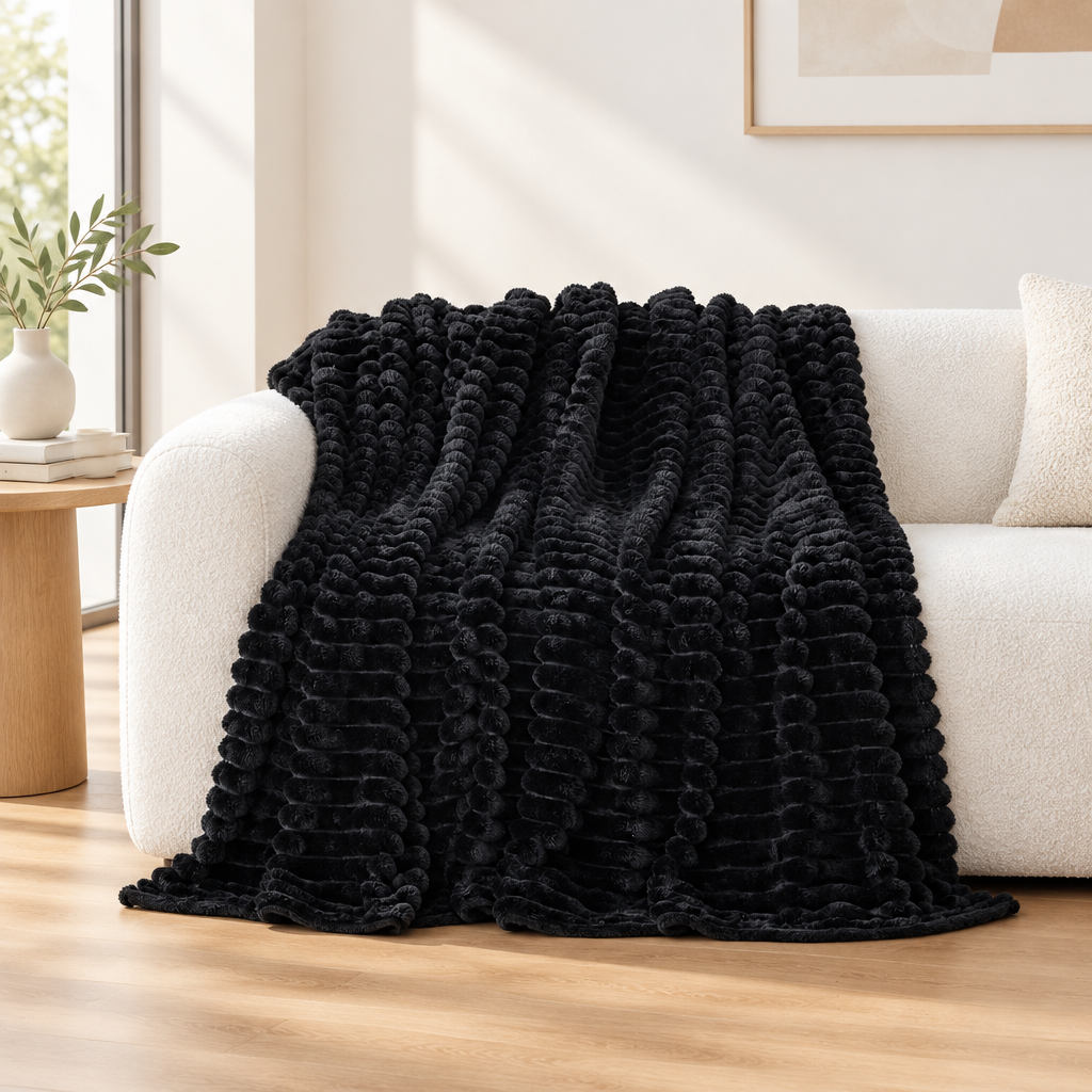 A black textured throw blanket with a ribbed, corded surface draped over a cream-colored sofa in a bright, modern living room.