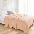 Beige plush blanket on a white bed with a grey cushion