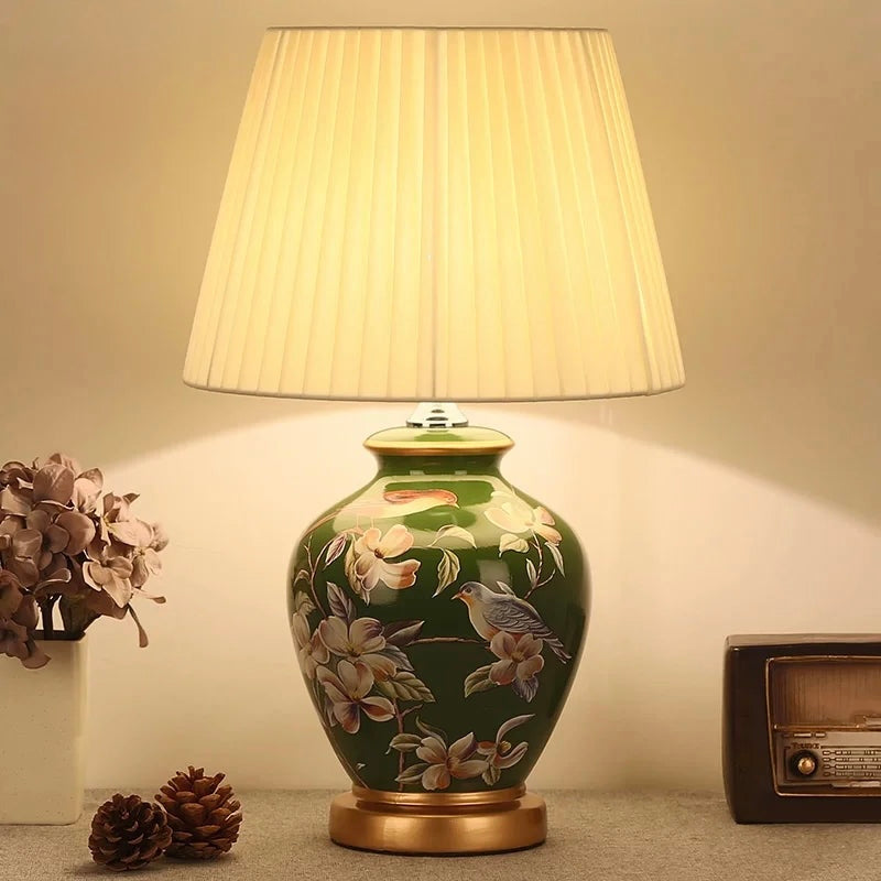 Green ceramic table lamp with bird and magnolia floral design, and pleated cream shade