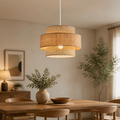 A modern two-tier pendant light with woven natural fiber shades hangs over a wooden dining table in a warm, neutral-toned dining room.