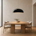 A modern dining room scene featuring a light oak wood dining table with six upholstered chairs, a black dome-shaped pendant light, and a small bowl of greenery on the table.