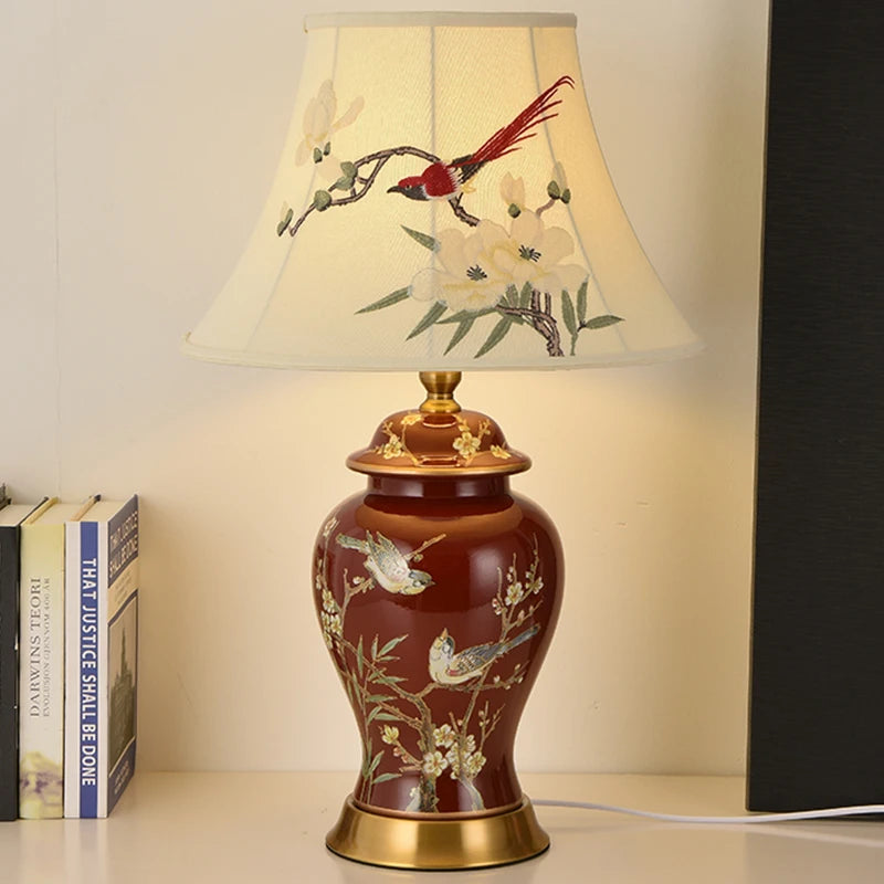 Decorative table lamp with floral and bird design on a white surface.