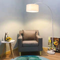 A white arc floor lamp overhanging a grey armchair in a cosy living room setting.