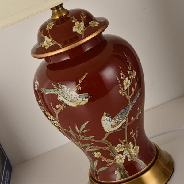 Decorative red vase with bird and floral patterns on a white surface.