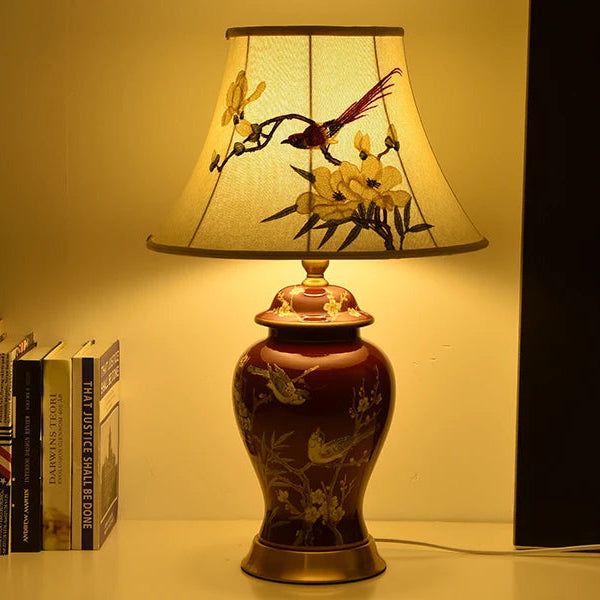 Decorative lamp with floral and bird design on a table next to books.