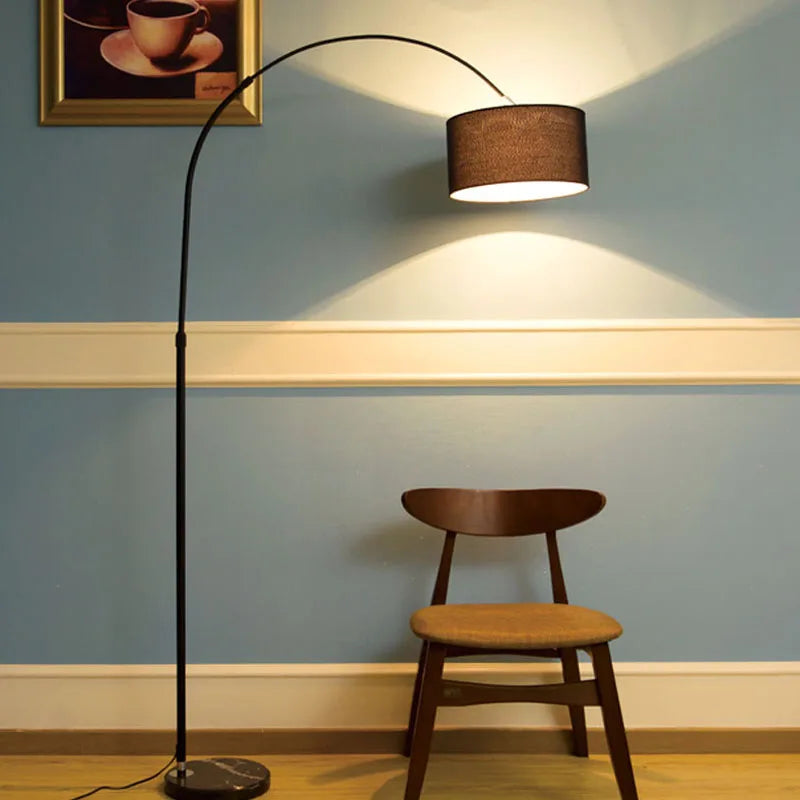 A black arc floor lamp overhanging a wooden chair against a blue wall.