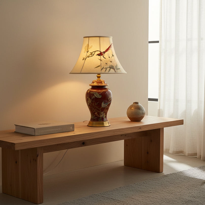 Decorative lamp on a wooden table with a book and small vase in a softly lit room.