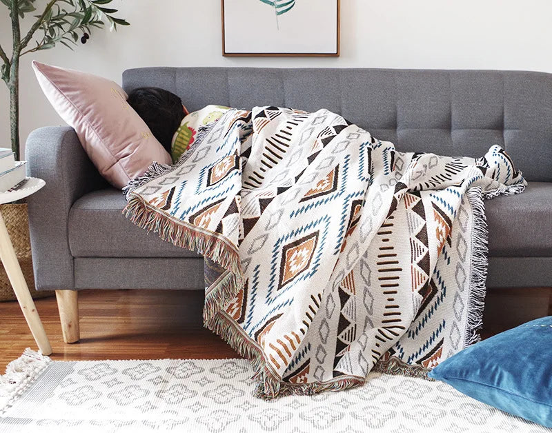 Patterned throw blanket draped over a gray sofa in a living room setting.
