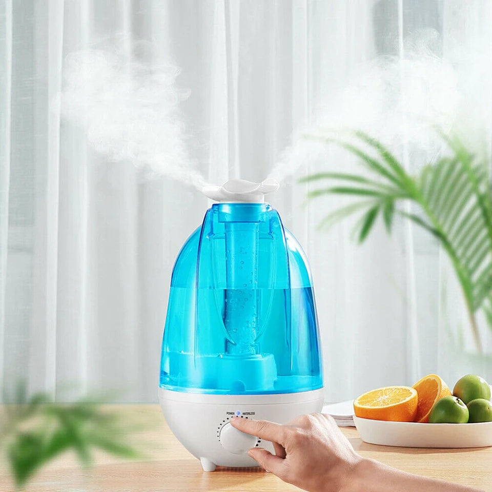 Blue and white humidifier on a table with a hand adjusting it, surrounded by fruits and plants.