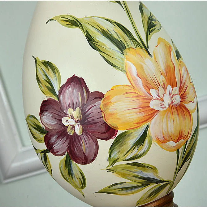 Hand-painted floral resin table lamp on a wooden nightstand beside an antique-style picture frame