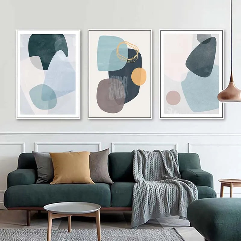 Set of three abstract geometric canvas prints styled above a dark green sofa in a modern living room