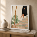 Illustrated canvas print of stacked books with a person standing above them beside monstera leaves.