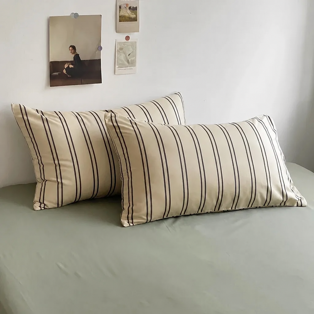 Two striped pillows of beige and black on a bed with a neutral colour scheme.