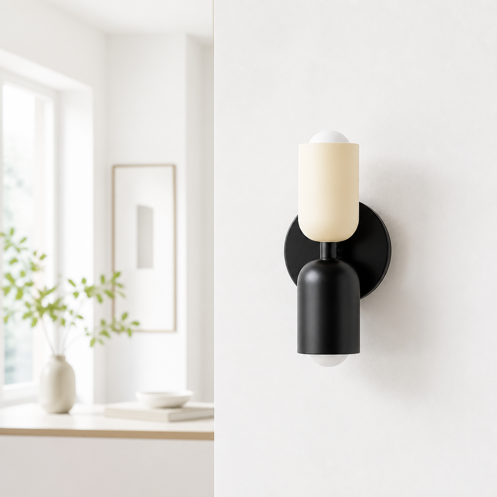 A modern wall sconce light fixture with a matte black metal body and a frosted cream glass shade, mounted on a white wall in a bright, minimalist interior setting.