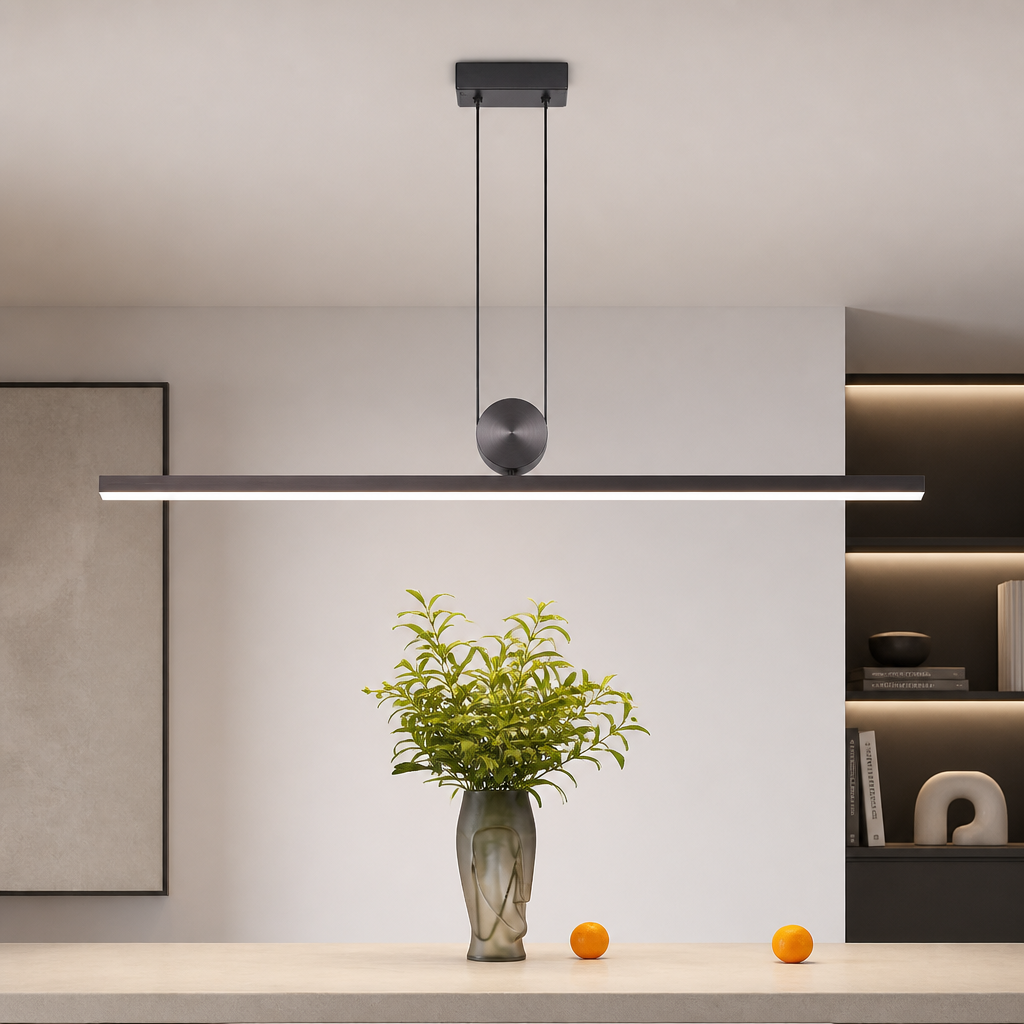 A modern linear LED pendant light with a matte black finish and a central spherical accent, suspended over a dining table with a vase of greenery in a minimalist interior setting.