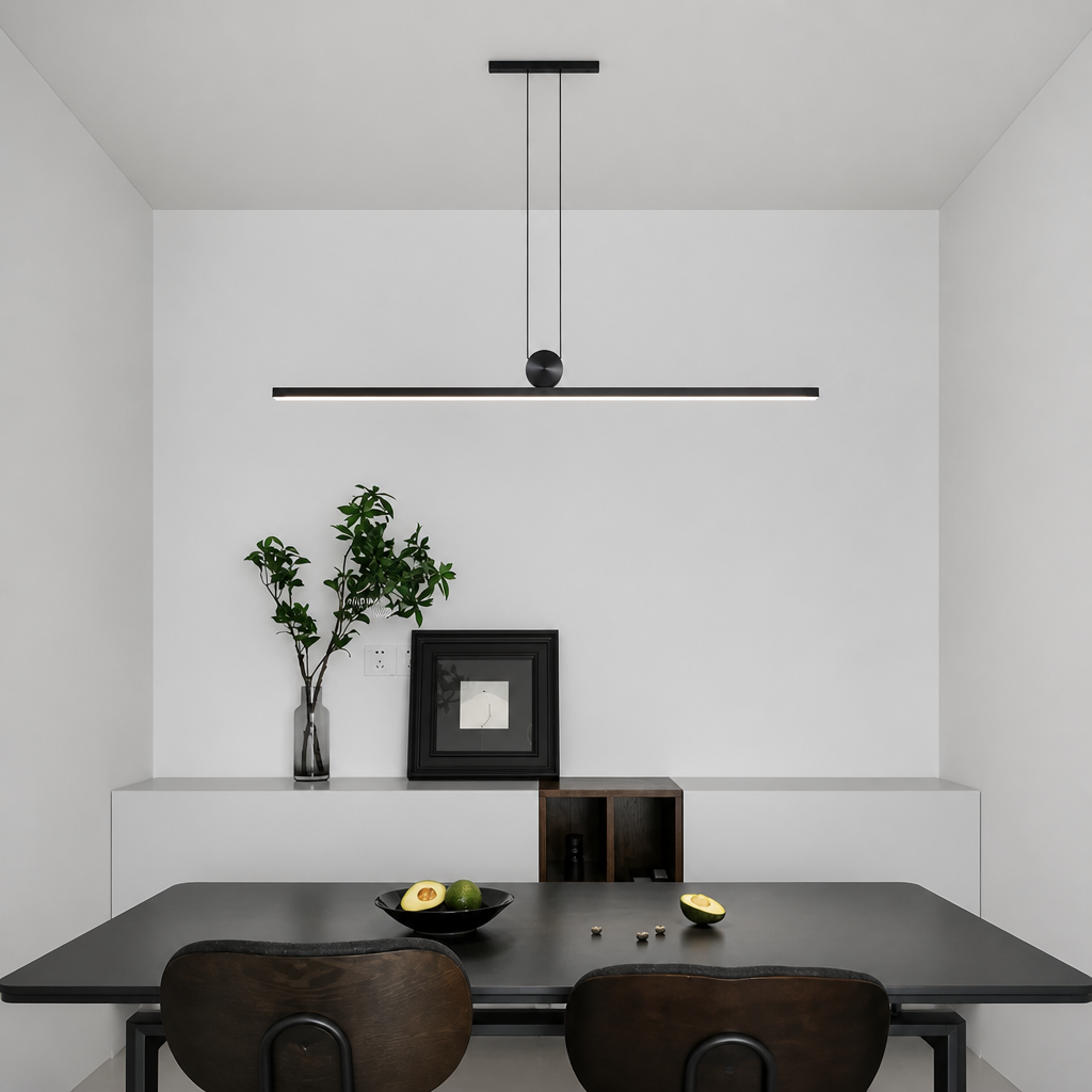 A minimalist modern linear pendant light in matte black hangs above a dark dining table with two wooden chairs in a clean, contemporary dining room setting.
