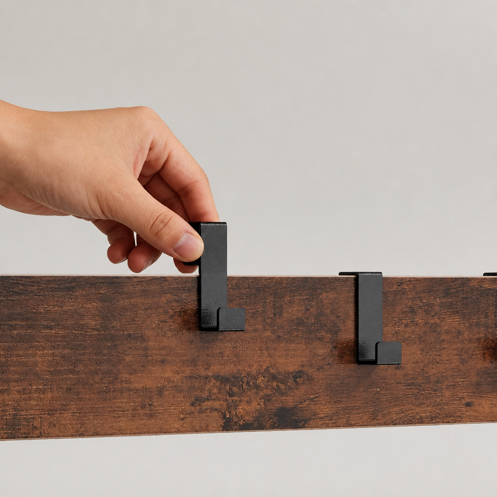 A hand is shown attaching a black metal wall hook to a dark brown wooden rail against a light gray background.