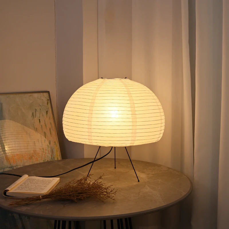 Round table with a dome lamp, book, and decorative branch against a neutral wall.