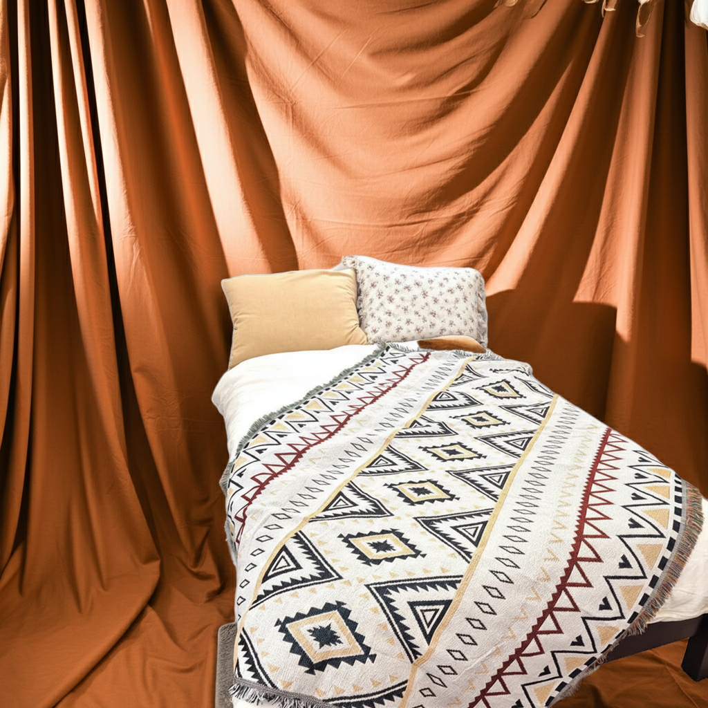 Bed with patterned blanket and pillows against a brown curtain backdrop