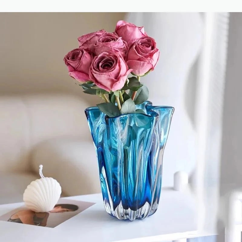 Blue and clear glass vase with pink roses on a white surface