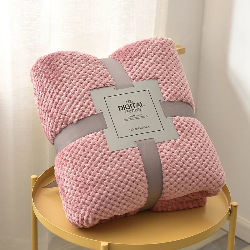 Pink textured blanket with a label on a yellow stool against a white curtain background