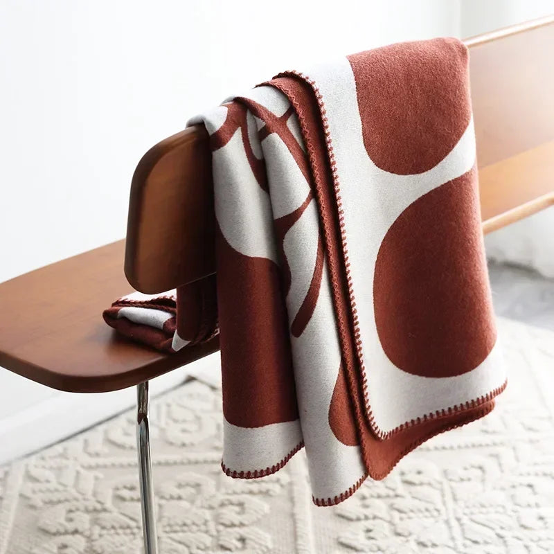 Rust and cream abstract jacquard blanket with blanket stitch edge draped over a wooden chair on a textured cream rug