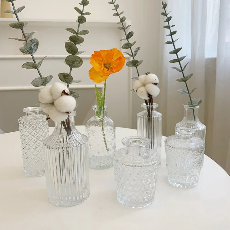 Clear glass vases with decorative plants and flowers on a white surface.