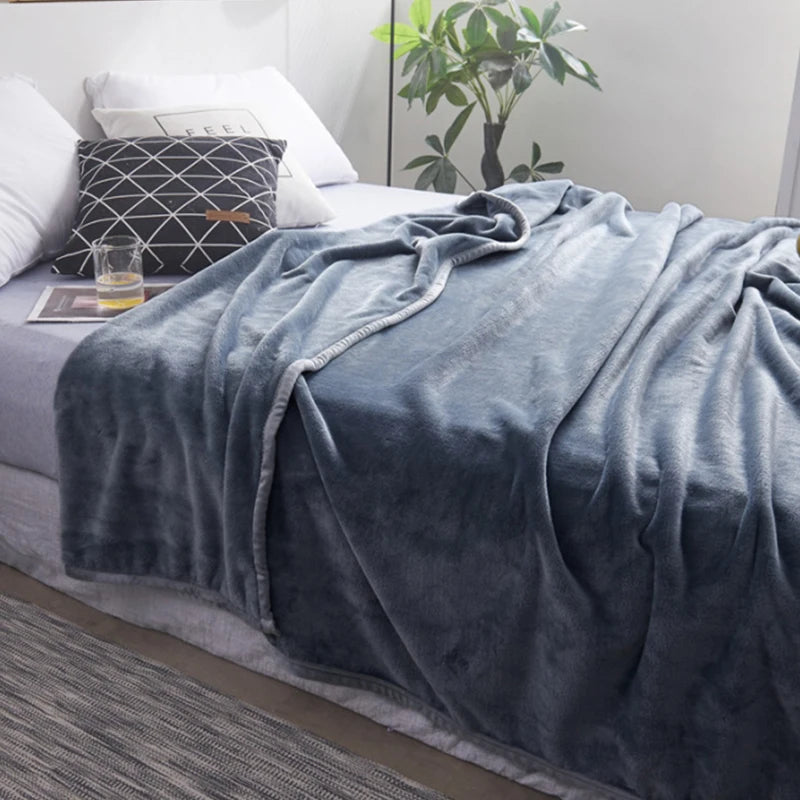 Grey blanket draped over a bed in a bedroom setting with a plant and pillows.