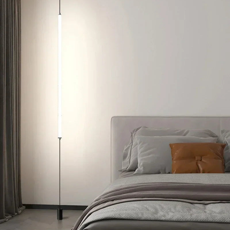 Slim floor-to-ceiling LED lamp beside a modern bedroom setting