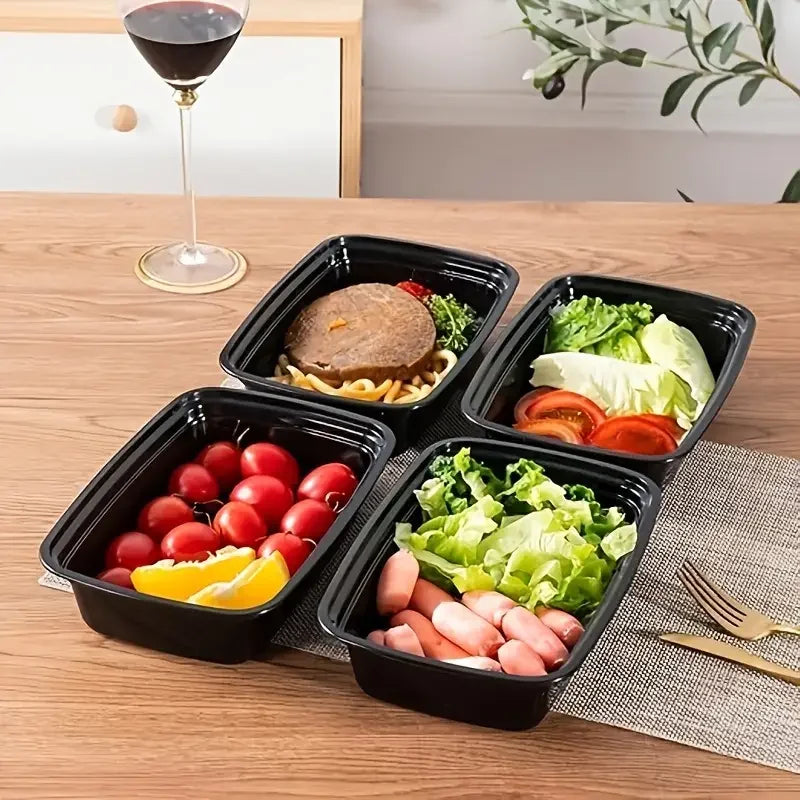 Four black meal prep containers with food on a wooden table with a glass of red wine.