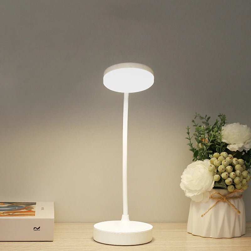 White LED desk lamp on a wooden surface with a vase of flowers in the background