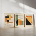 A curated 3-piece Bauhaus canvas art collection featuring geometric circles and blocks in sage green and ochre, leaning against a minimalist white wall.