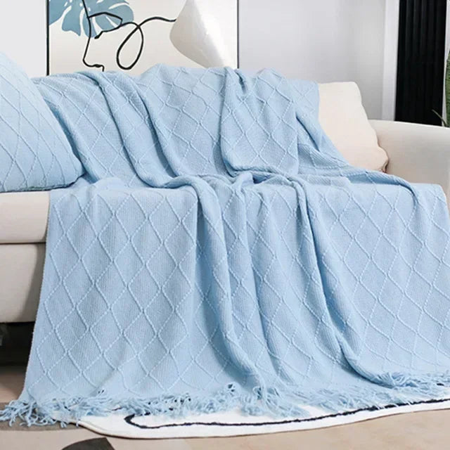 Light blue knit throw with a raised diamond pattern and fringed edge resting on a cream sofa