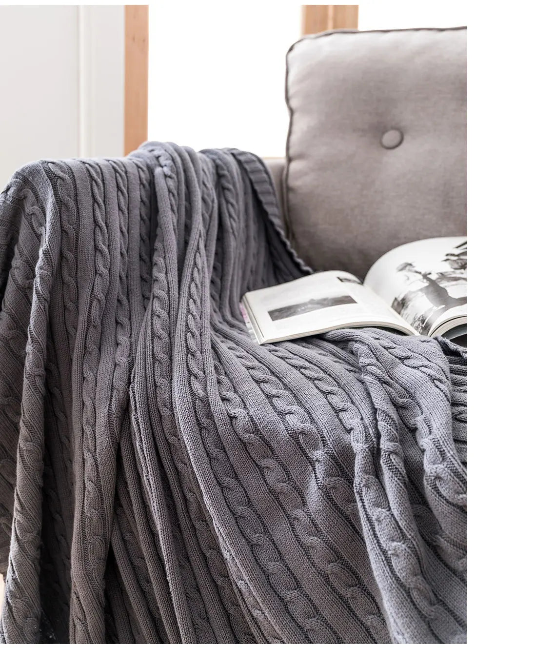 Grey cable knit blanket draped over a sofa with a book underneath