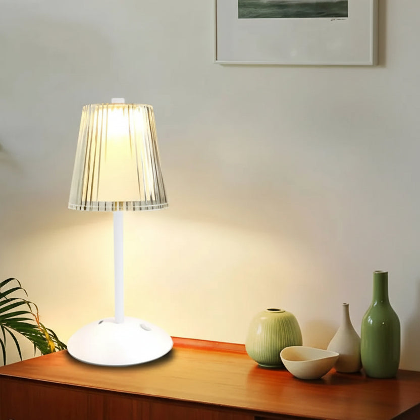 Table lamp on a wooden surface with a plant and decorative items in the background.