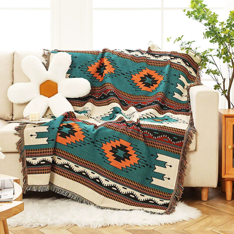 Teal Aztec throw blanket draped over a cream sofa with a daisy-shaped cushion