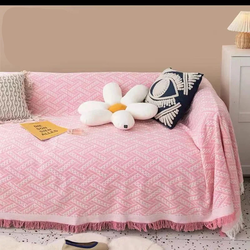 Pink blanket on a sofa with decorative pillows and a lamp in a room.