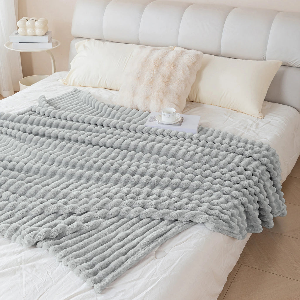 Gray textured blanket on a bed with white pillows and a tufted headboard.