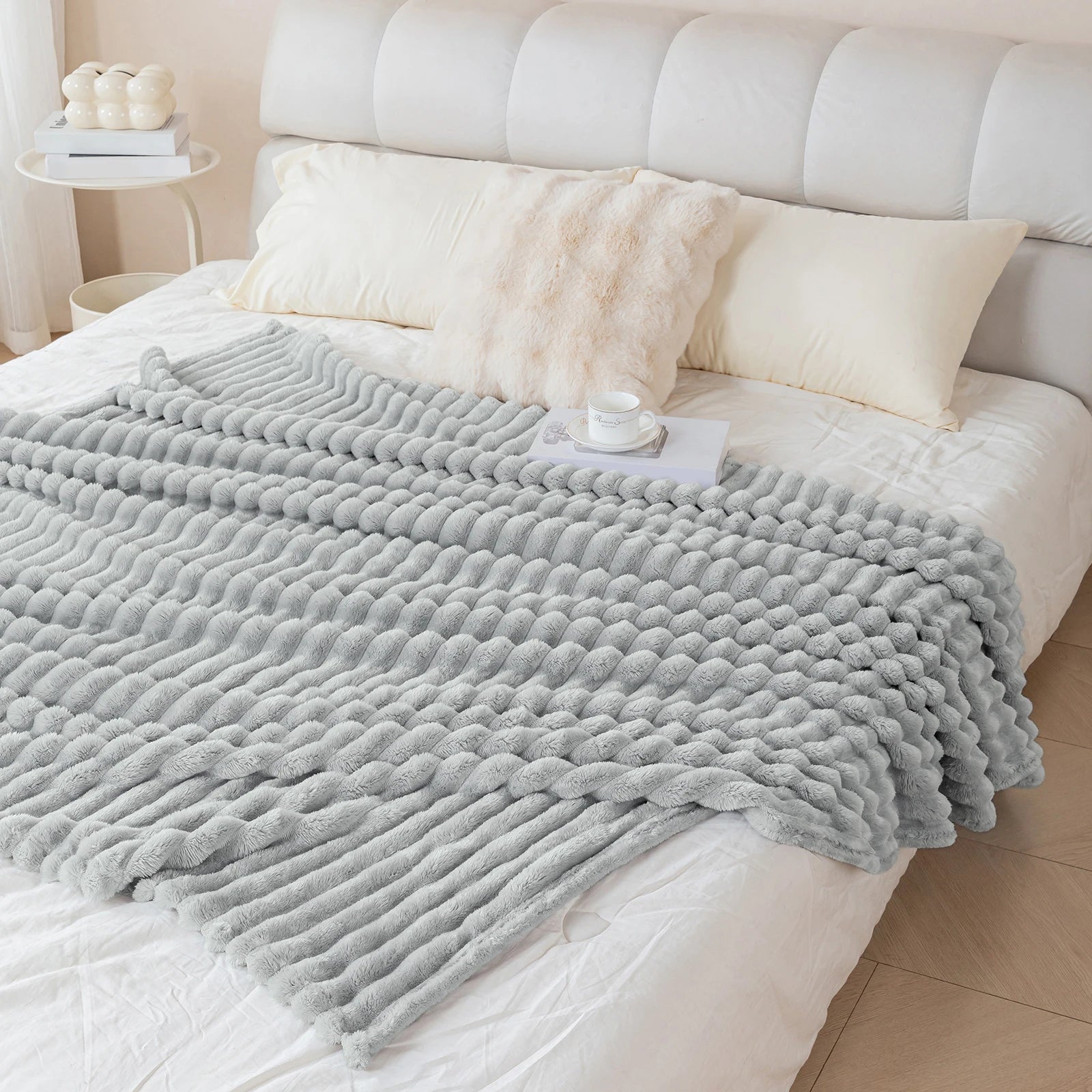 Gray textured blanket on a bed with white pillows and a tufted headboard.