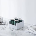White can holder with four green cans on a marble surface with books and a coffee cup in the background.
