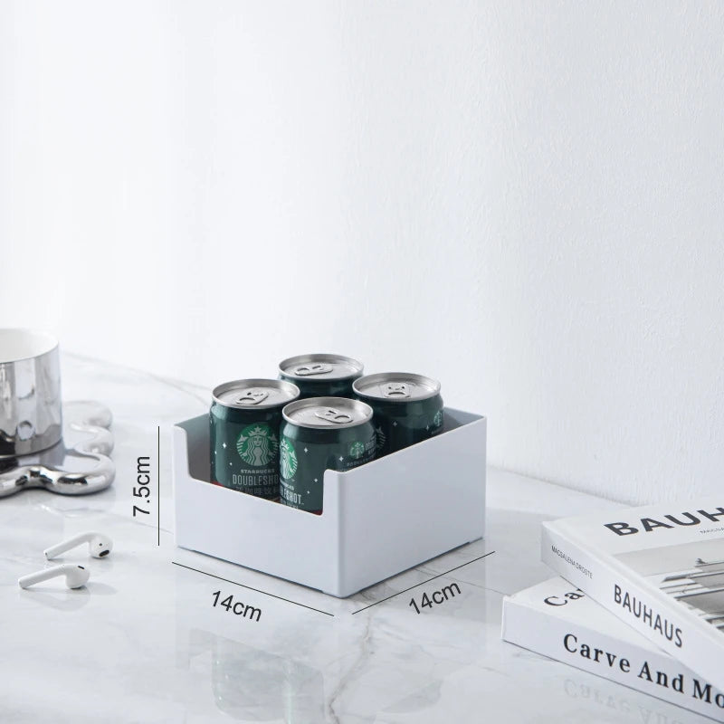 White can holder with four green cans on a marble surface with books and a coffee cup in the background.