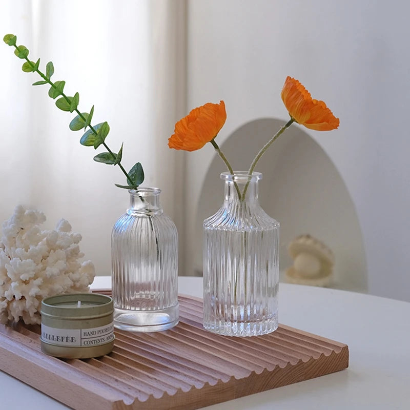 Two small glass vases with orange flowers on a wooden tray with a white background
