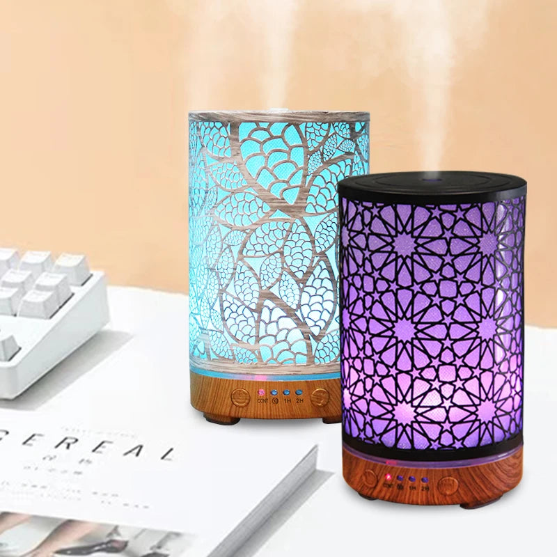 Two essential oil diffusers on a white desk, one glowing blue and one glowing purple, showing cool mist output.