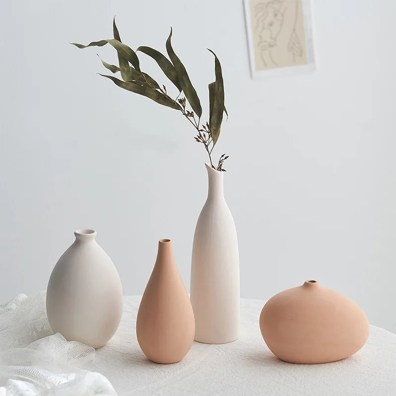 Four ceramic vases of different shapes and colors on a light surface with a neutral background.
