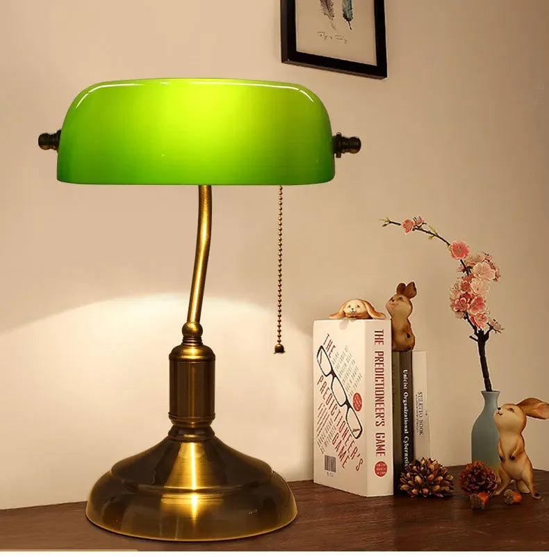 Green glass banker-style desktop lamp with antique brass metal base and pull-chain detail