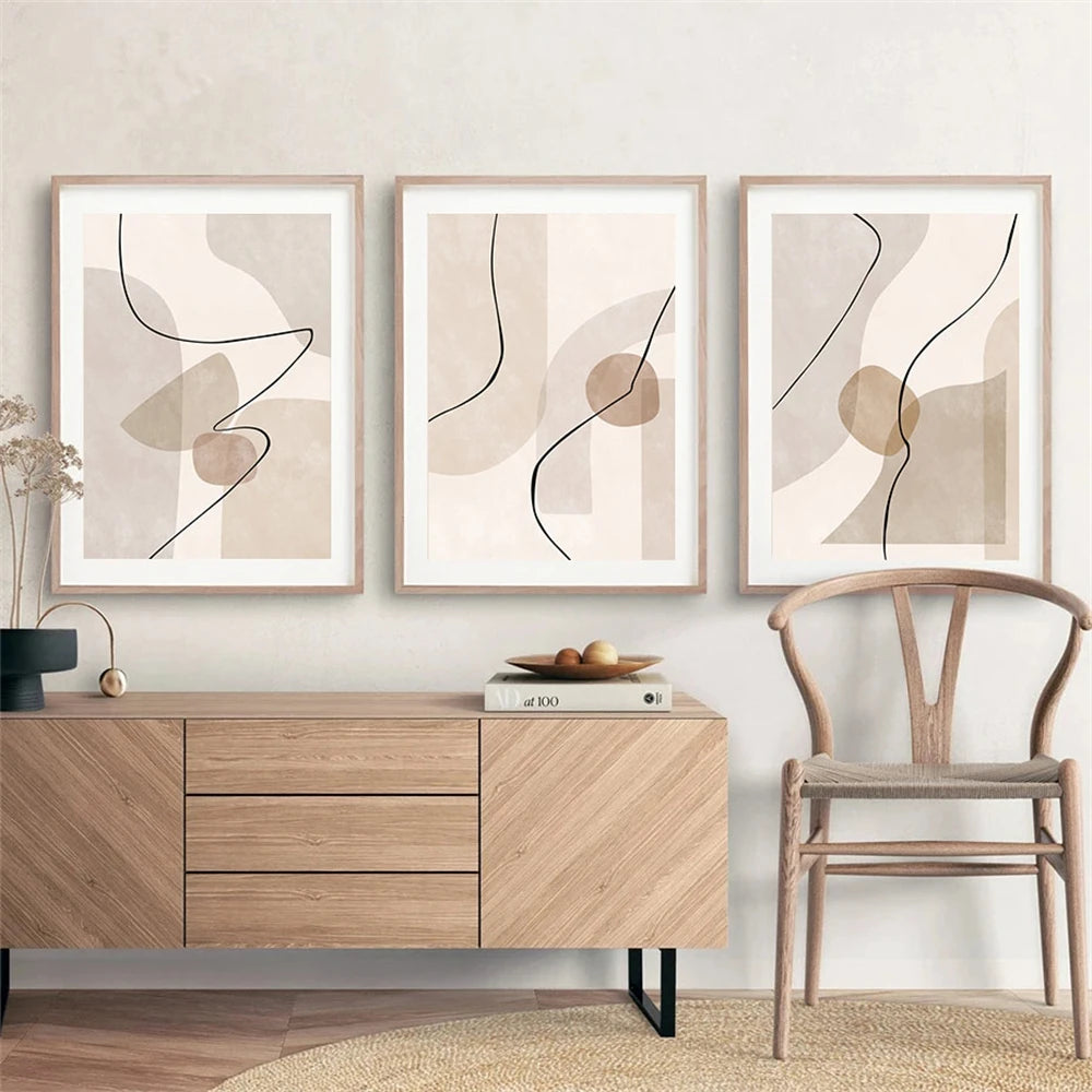 Three abstract art pieces on a wall above a wooden cabinet with a chair in the foreground.